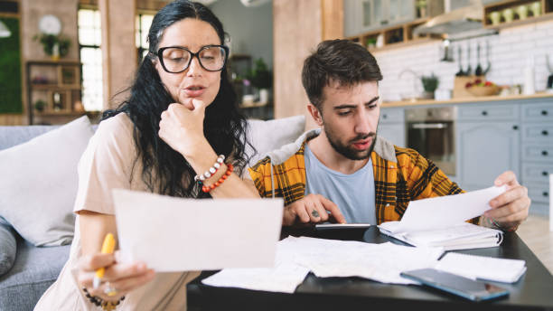 istock Couple calculating bills at home using calculator.  Couple checking bills and documents while calculating finances sitting in the living room. Man and woman at home analyzing their finance with documents. 1423253932