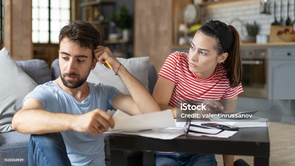 Frustrated concerned young couple calculating overspend budget, doing paperwork job at laptop, talking about financial problems, insurance, mortgage, fees, loan conditions, bankruptcy, economic inflation Currency Stock Photo