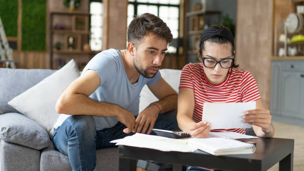 istock Young couple calculating bills at home using calculator.  Couple checking bills and documents while calculating finances sitting in the living room. Man and woman at home analyzing their finance with documents. 1423253940