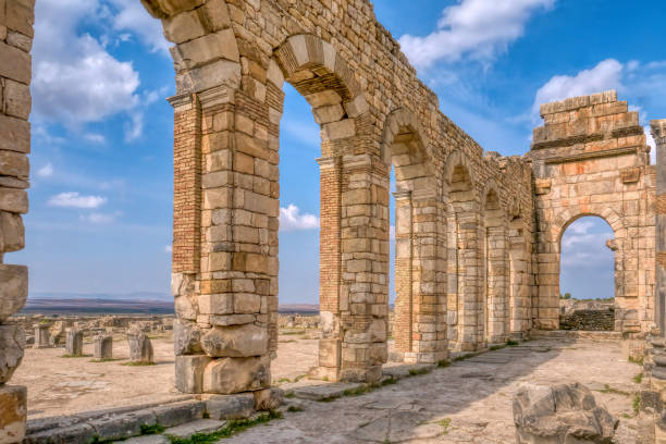 Restored basilica wall at Volubilis Roman ruins in Morocco. The brick and stone arched exterior wall of the basilica at ancient Roman site near Meknes, on a sunny day with blue sky. meknes stock pictures, royalty-free photos & images