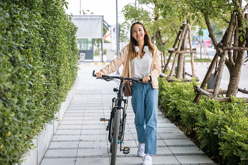 Happy female smiling walk down the street with her bike on city road, ECO environment, Lifestyle Asian young woman walking alongside with bicycle on summer in countryside outdoor, healthy travel