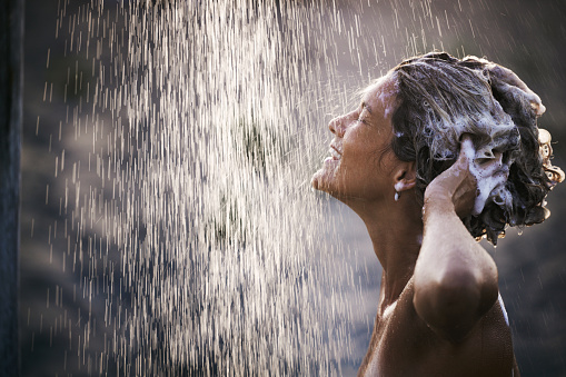 Profile view of happy woman enjoying while washing her hair with shampoo at outdoor shower. Copy space.