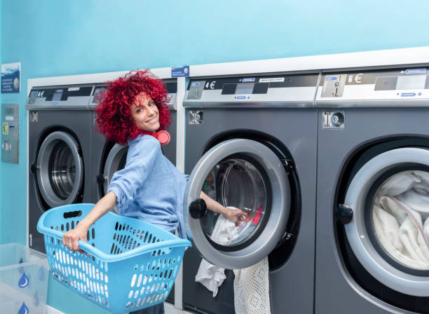 A smiling young woman with red afro hair doing laundry in a blue automatic laundromat
