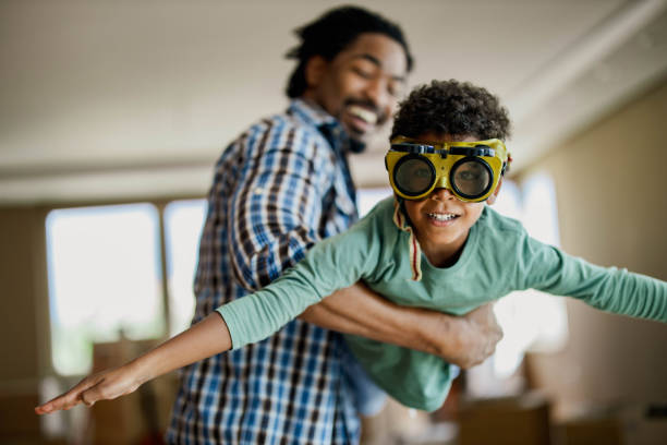 Happy African American boy pretending to be an airplane while having fun with his father and looking at camera.