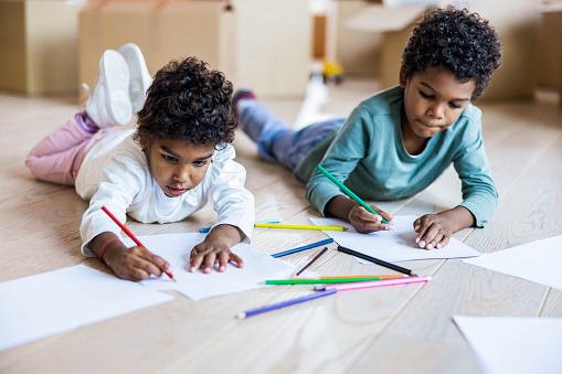 Small black siblings enjoying while drawing on the floor at their new apartment.