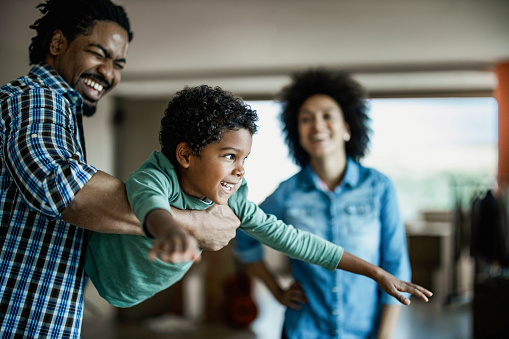 Happy black boy having fun while playing with his father at home. Woman is in the background.