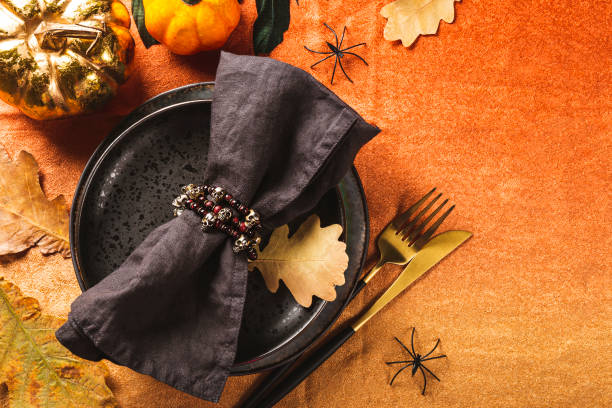 istock Halloween table setting concept. Black plate, golden cutlery, pumpkins, spooky Halloween decorations and autumn leaves on the table with an orange tablecloth, top view, close up 1423274792