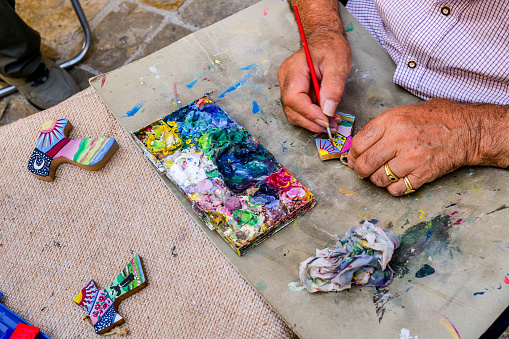 Assisi, Umbria, Italy, August 30 -- The hands of a craftsman paint a crucifix along an alley in the medieval heart of Assisi, in Umbria.