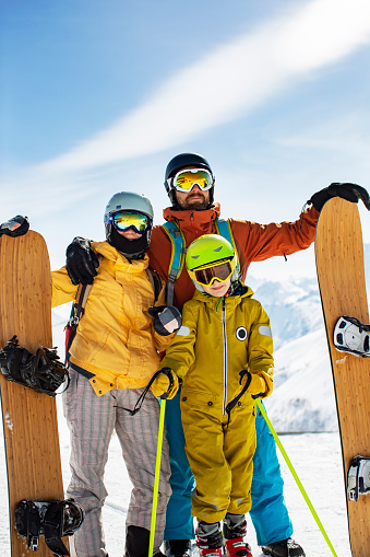 Laughing family in winter vacation with ski sport on snowy mountains. Happy man and woman with sons having fun and looking at camera. Family with two children enjoying winter holiday at ski resort.