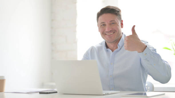 istock Man Showing Thumbs Up Sign While using Laptop in Office 1423281120