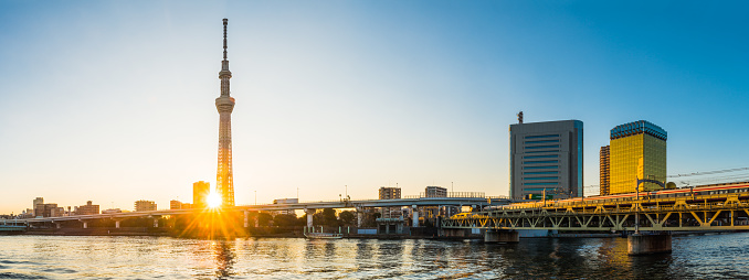 Golden light of sunrise glittering through the elevated highways along the Sumida River beside the iconic spire of the Tokyo Skytree in the heart of Japan’s vibrant capital city.