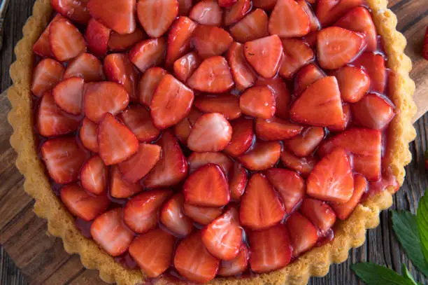 Background image with a  fresh baked strawberry tart  and glaze on wooden table. Top view