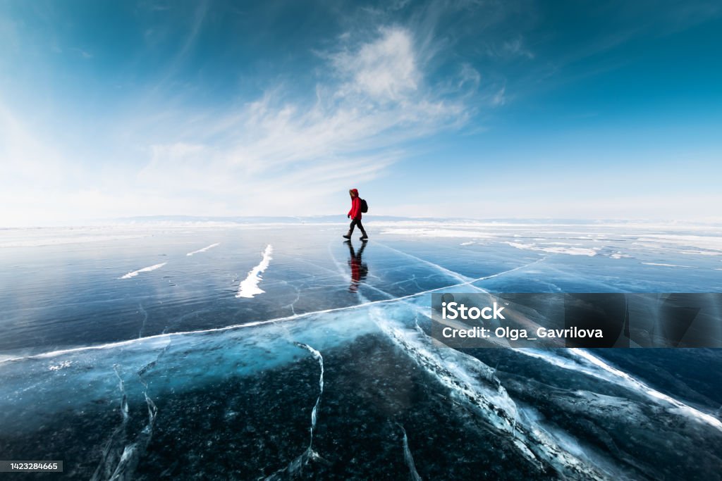 Man tourist walking on the ice of Baikal lake. Winter landscape of Baikal lake, Russia Man tourist walking on the ice of Baikal lake. Winter landscape of Baikal lake, Siberia, Russia. Blue transparent cracked ice and the blue sky. Winter Stock Photo