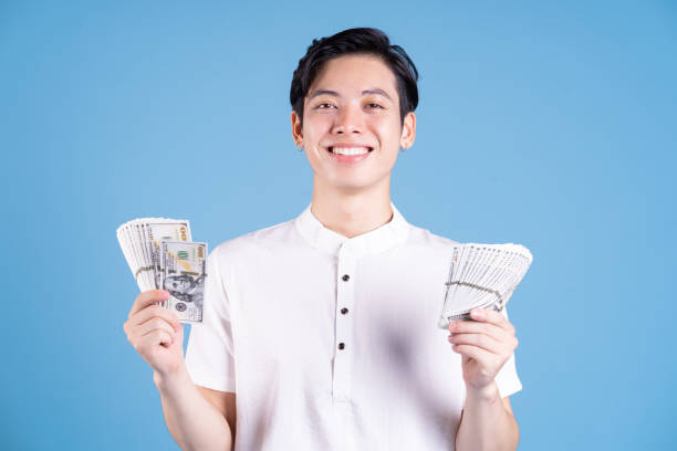 istock Young Asian man holding money on background 1423285378