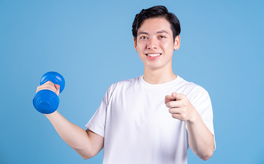 Young Asian man holding dumbbell on background