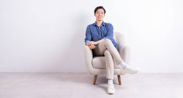 istock Young Asian man sitting on armchair on white background 1423285461