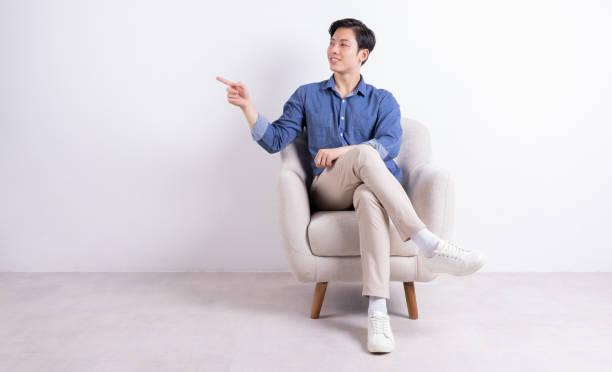 istock Young Asian man sitting on armchair on white background 1423285480