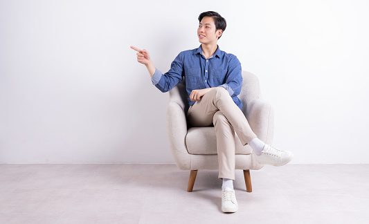 Young Asian man sitting on armchair on white background