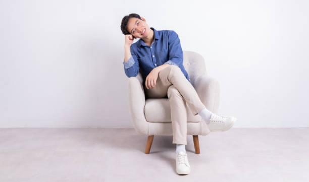 istock Young Asian man sitting on armchair on white background 1423285481