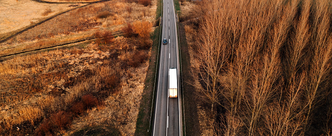 Aerial shot of semi truck and car driving along the highway through autumn scenery landscape, drone pov high angle view