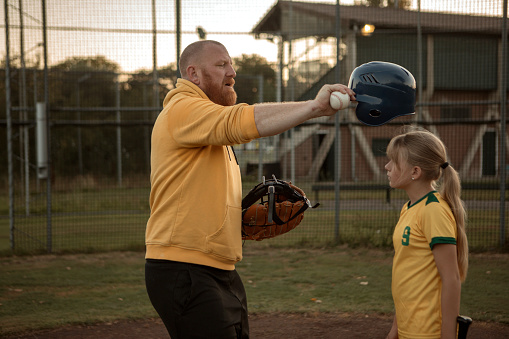 Middle Aged Redhead Father working hard during a baseball coaching session for his daughter at a training pitch on a sunny day