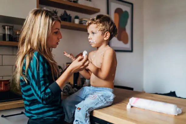 The little boy has red rashes all over his body, so his mother applies measles medicine to him
