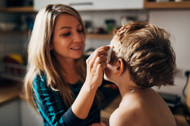 taillenansicht einer lächelnden mutter, die windpockenmedikamente auf ihren sohn aufträgt - waistup stock-fotos und bilder