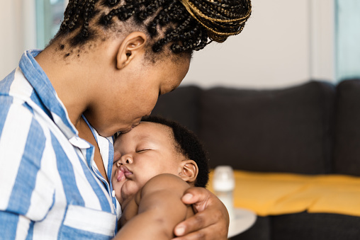 Portrait of a happy African American woman holding her cute baby boy and enjoying motherhood at home