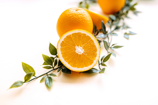 Whole and sliced orange with plant leaves on a white background