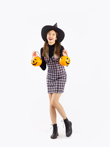 Pretty asian woman in halloween costume wearing witch hat holding and carrying orange pumpkin bucket and lantern on white background. Full body girl.