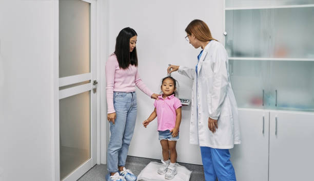 소아과 의사는 상담을 위해 어머니와 함께 의료 클리닉에 어린이를 방문하는 동안 아시아 여성 어린이의 신장을 측정합니다. 소아과 - tall human height women measuring 뉴스 사진 이미지