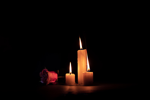 three lighted candles next to a rose on a black background