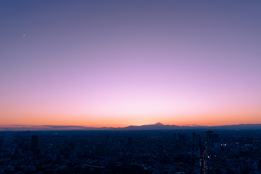 The sky with beautiful gradation of twilight time and the moon floating in it. Fuji and the city of Tokyo in silhouette.