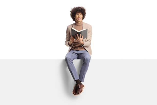 Elegant young man with curly hair sitting on a panel and holding a book stock photo
