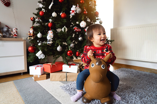 Toddler girl Japanese ethnicity riding a horse toy during Christmas morning