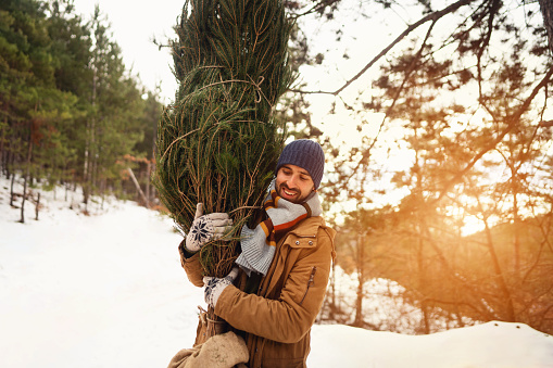 Portrait of excited young Caucasian man carrying a Christmas tree, he found in forest
