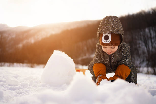 Playful Caucasian toddler making a snowman in nature