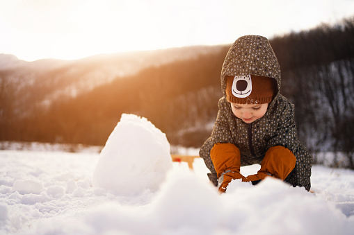 Playful Caucasian toddler making a snowman in nature