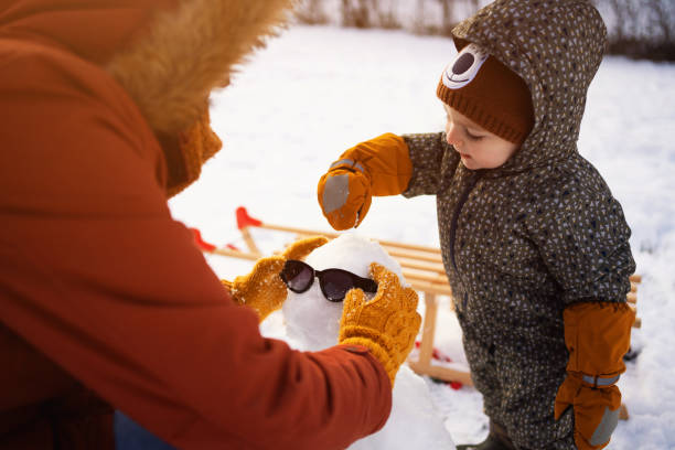 Caucasian mother and son, together making a snowman in the nature