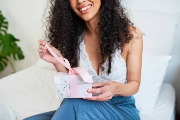 istock Close up of young woman pulling open ribbon on gift box in bed 1423311638
