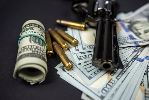 gun and bullet shells next to American dollar bills on a black background. Concept of crime and law. Criminal money and punishment.
