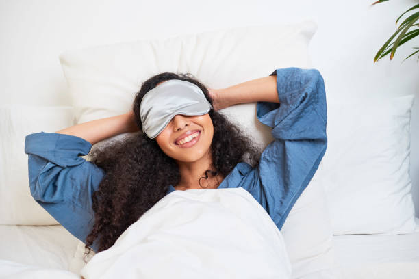 A young multi-ethnic woman stretches with arms behind head and sleep mask A young multi-ethnic woman stretches with arms behind head and sleep mask. High quality photo hair on pillow stock pictures, royalty-free photos & images
