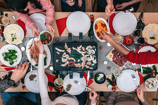 overhead view on family sitting around wooden table with raclette grill