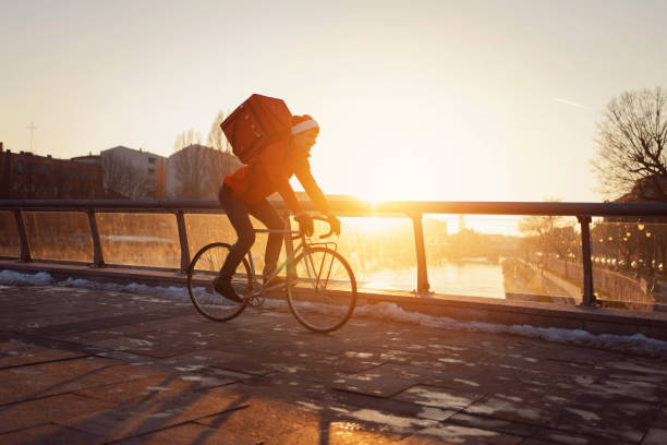 istock Unrecognizable delivery person riding bicycle through city, during sunset 1423316994