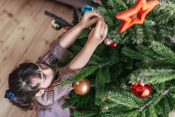 Photo of little girl decorating christmas tree with colorful glass balls
