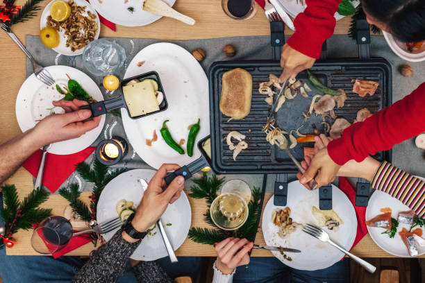 семья готовит различные блюда на гриль раклетт на деревянном столе - raclette cheese стоковые фото и изображения