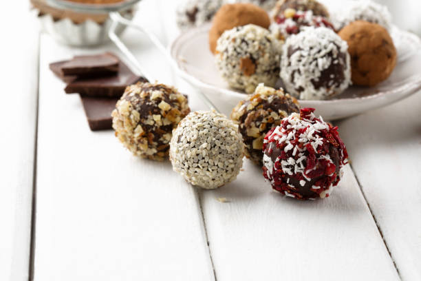 Homemade sugar free Chocolate Candy Balls with Cocoa Powder and Nuts Homemade no added sugar, sugar free Chocolate Candy Balls with cocoa powder, coconut, berries and chopped hazelnuts on white wooden background. Healthy eating concept. plasma ball stock pictures, royalty-free photos & images