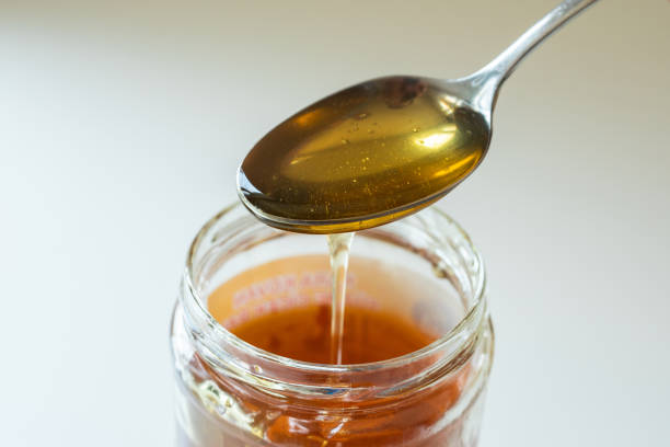 glatter goldener honig, der vom löffel im glas fällt - syrup jar sticky isolated objects stock-fotos und bilder
