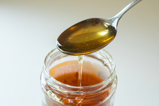 Smooth golden honey dropping from spoon in jar