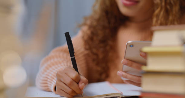 istock Student, education and online learning woman writing notes while doing research on a phone. Closeup female studying with study apps for assignment or preparing for college, university or school exams 1423321220